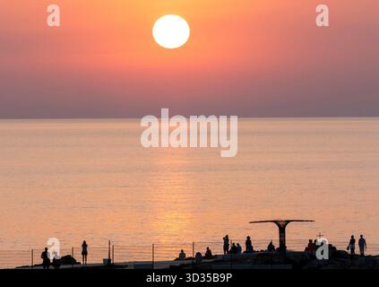 I turisti guardano il sole tramontare dal sentiero costiero, Paphos, Cipro. Foto Stock