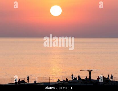 I turisti guardano il sole tramontare dal sentiero costiero, Paphos, Cipro. Foto Stock