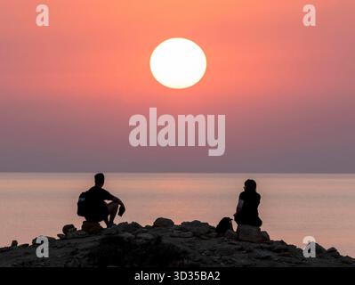 Una coppia guarda il sole tramontare da un punto panoramico sulla costa di Paphos, Cipro. Foto Stock