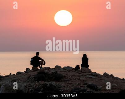 Una coppia guarda il sole tramontare da un punto panoramico sulla costa di Paphos, Cipro. Foto Stock