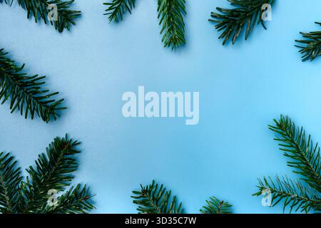 Vista superiore dei rami di abete verde disposti intorno ai bordi su uno sfondo blu con spazio di copia. Composizione invernale e natalizia minima per il saluto Foto Stock