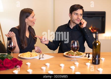 Tensione durante la cena mentre la coppia discute con un partner al telefono in un ambiente romantico Foto Stock