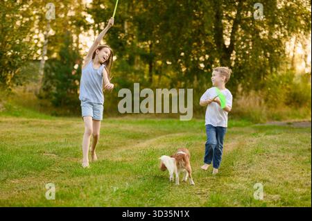 I bambini trascorrono del tempo all'aperto, giocando all'aria aperta, divertendosi, correndo a piedi nudi con la rete nell'erba, giocando all'aperto con il cane. COU Foto Stock