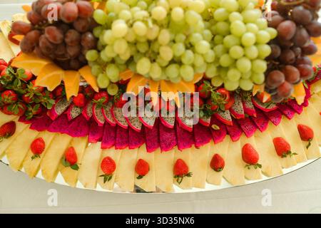 Un vivace assortimento di frutta e formaggi è splendidamente disposto su un grande vassoio, che mostra uva, fragole, frutta di drago e vari formaggi Foto Stock