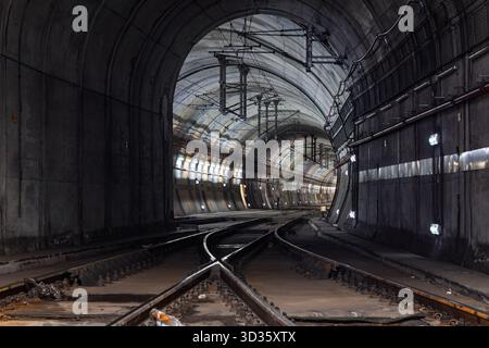 Un lungo tunnel buio con binari convergenti e linee elettriche aeree, che conduce all'uscita della storica stazione ferroviaria di Rossio. Foto Stock