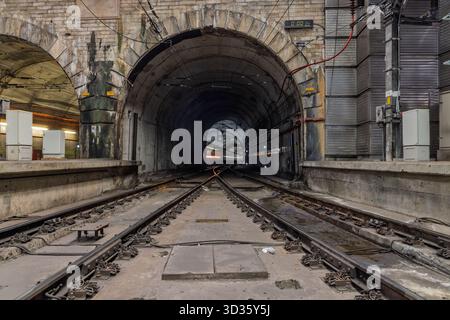 L'ingresso al tunnel della stazione ferroviaria di Rossio presenta un arco in pietra e binari ferroviari che conducono all'oscuro passaggio sotterraneo. Foto Stock