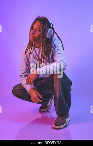Giovane che ascolta musica indossando cuffie in un vivace studio Foto Stock