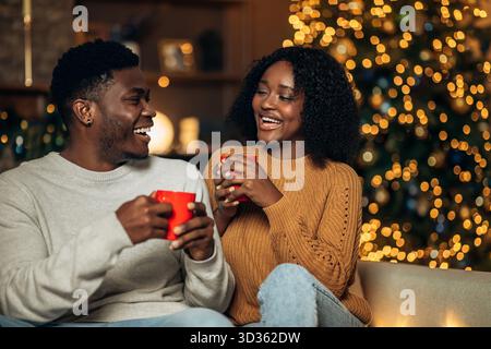 La giovane coppia gode di un'accogliente vigilia di Natale con bevande calde nel soggiorno splendidamente decorato Foto Stock