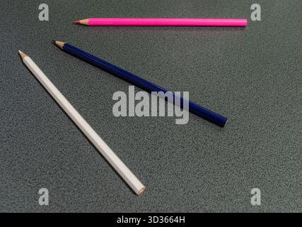 Tre matite colorate, rosa, blu e bianco, disposte diagonalmente su una superficie grigia. Composizione minimalista che rappresenta creativi Foto Stock