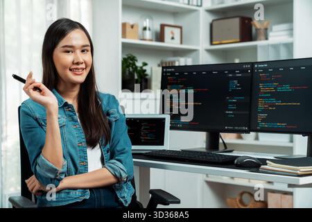 Giovane sviluppatore asiatico in IT che guarda la fotocamera per presentare informazioni online su pc con applicazione dati del programma di codifica, indossando una camicia jeans Foto Stock