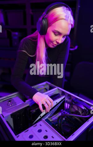 Una giovane donna che gioca aggiorna un PC per videogame, personalizzando l'hardware con particolare attenzione in una configurazione high-tech Foto Stock