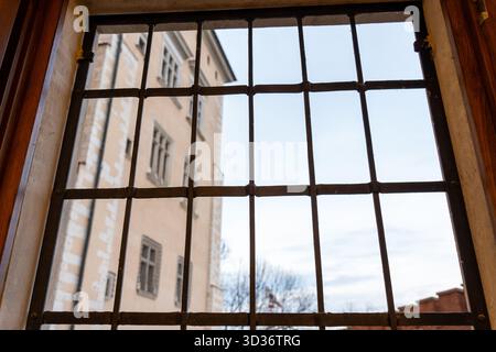 Vista attraverso le vecchie finestre in metallo che mostrano la facciata dell'edificio storico e il cielo nuvoloso che rappresenta sentimenti di confinamento e desiderio di libertà. Conce Foto Stock