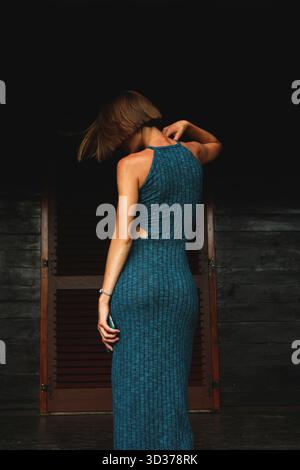 Donna irriconoscibile con un abito lungo in piedi dietro la fotocamera su uno sfondo scuro. Ritratto completo del profilo del corpo di un bellissimo modello sottile. Foto Stock