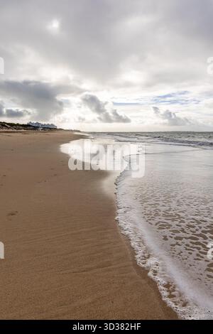 Spiaggia sabbiosa sulla costa atlantica. Vista dello skyline di Rota, cielo nuvoloso sulla spiaggia Playa de la Costilla, Costa de la Luz, Cádiz, Andalusia, Spagna. Foto Stock