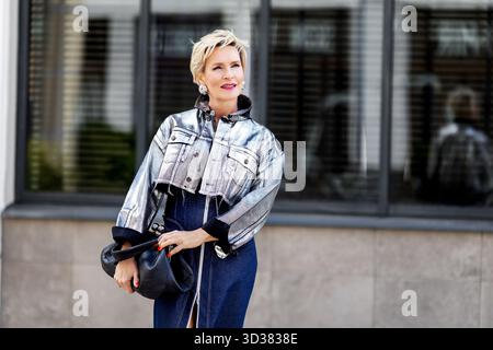 Donna con capelli biondi corti in giacca metallizzata e gonna in denim. Stile urbano alla moda con accessori di tendenza. Donna matura moderna Foto Stock