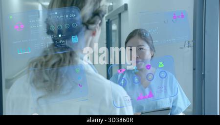 Due professionisti che indossano scrub che esaminano i dati olografici sul pannello nel corridoio dell'ospedale Foto Stock