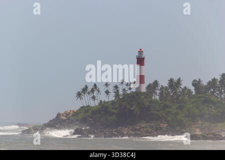 Suggestivo faro rosso e bianco su un lussureggiante promontorio dell'isola coperto di palme Foto Stock