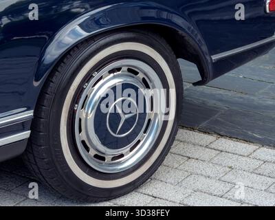 COLOMBRES, SPAGNA - 12 LUGLIO 2025: Primo piano di un classico cerchio Mercedes-Benz con coprimozzo cromato su un'auto vintage blu scuro. Design automobilistico rétro, lu Foto Stock