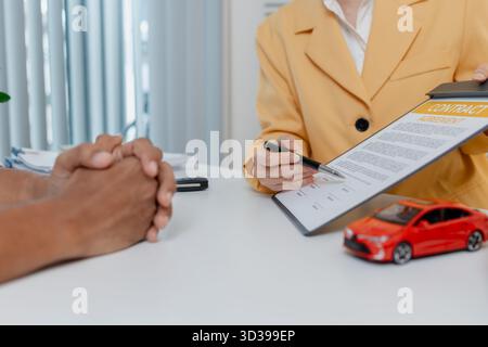Una negoziazione per la vendita di auto si svolge in un ufficio in cui una donna venditrice con un blazer giallo spiega i dettagli di un contratto a un cliente maschio, showin Foto Stock