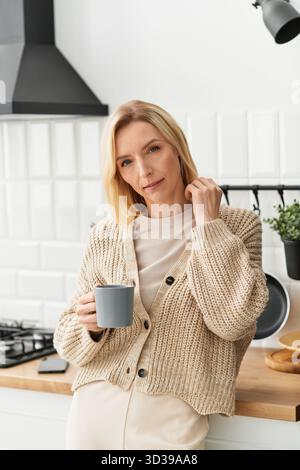 Una donna bionda si rilassa nel suo accogliente appartamento, sorseggiando un tè e godendosi la calda atmosfera di comfort. Foto Stock