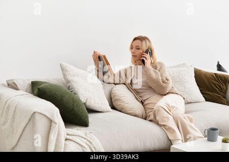 Una donna bionda si rilassa su un comodo divano nel suo accogliente appartamento, chiacchierando al telefono. Foto Stock