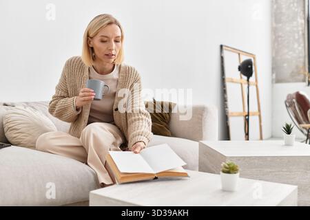 Una donna bionda si rilassa a casa, gustando un tè e leggendo in un intimo abbigliamento invernale. Foto Stock