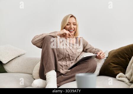 Una donna si rilassa nel suo elegante appartamento, indossando abiti morbidi e sorridendo mentre si diverte. Foto Stock