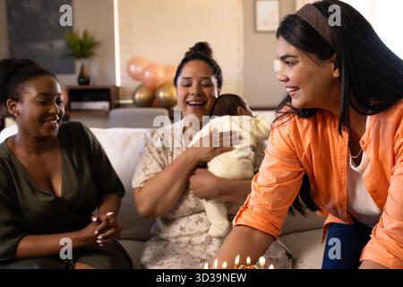Festeggiamo a casa, amici diversi che si godono il compleanno con una torta e un bambino. Festeggiamenti, feste, felicità, famiglia, insieme, amicizia || modello rilasciato Foto Stock