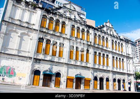 Vista ad ampio angolo di un lungo edificio storico di epoca coloniale caratterizzato da una facciata bianca ornata e file di impressionante, alto e luminoso arancione-giallo Foto Stock