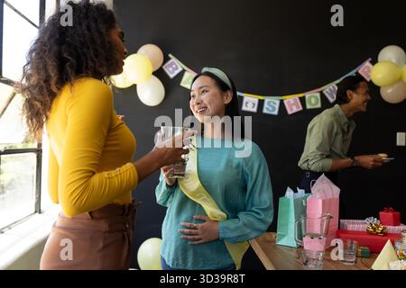 Festeggiamo la baby shower, amici diversi che si divertono con drink e risate a casa. Celebrazione, riunione, amicizia, bevande, diversità, felicità || modello rilasciato Foto Stock