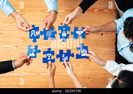 Gruppi diversi di persone che collaborano intorno a un tavolo di legno, collegando pezzi di puzzle che simboleggiano il lavoro di squadra e vari concetti di realizzazione e. Foto Stock