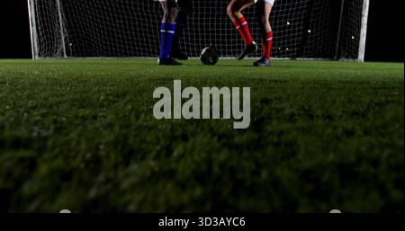 Sfida tra due giocatori maschi sul campo da calcio notturno, con erba, rete porta, scarpe da calcio Foto Stock