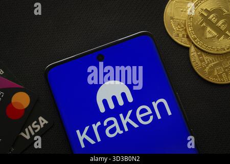 Dacca, Bangladesh- 26 agosto 2025: Smartphone con logo Kraken circondato da monete Bitcoin e carte di pagamento Foto Stock