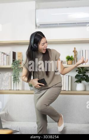 Una giovane donna che canta e balla energicamente a casa, mostrando il suo amore per la musica e l'espressione gioiosa in un ambiente elegante Foto Stock
