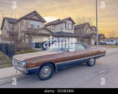 Calgary, Alberta, Canada. 20 aprile 2025. Una Chrysler coupé vintage marrone è parcheggiata in una strada suburbana di fronte alle case durante il tramonto, mostrando un c Foto Stock