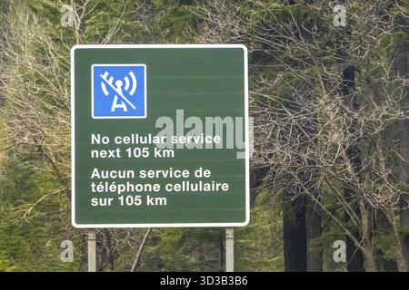 Banff, Alberta, Canada. 2 aprile 2025. Un cartello stradale verde avverte che non c'è nessun servizio cellulare dopo 105 km in inglese e francese, sullo sfondo di alberi Foto Stock