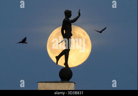 Hannover, Germania. 5 novembre 2025. La luna sorge all'orizzonte dietro la statua del "Torchbearer" (1937) sulla riva settentrionale del Maschsee. La sera, la più grande luna piena dell'anno può essere vista sulla Germania - una cosiddetta superluna. Credito: Julian Stratenschulte/dpa/Alamy Live News Foto Stock