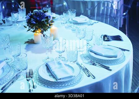 Cibo, splendido tavolo rotondo per banchetti con bicchieri di cristallo, fiore all'occhiello e candele, preparato per una cena formale o un ricevimento di nozze Foto Stock