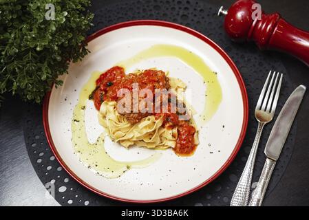Cibo, deliziose tagliatelle condite con succose polpette in una ricca salsa di pomodoro, guarnite con olio d'oliva e pepe nero Foto Stock