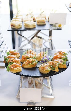 Cibo, vassoio nero rotondo con tartine di salmone affumicato su pane tostato, condito con panna e verdure, perfetto per il catering di lusso Foto Stock