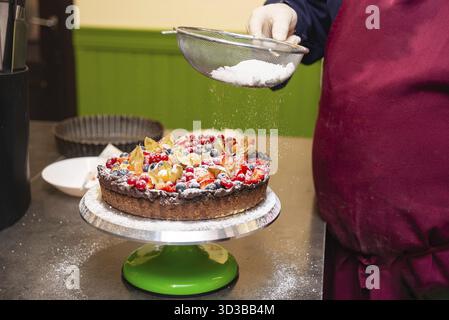Cibo, pasticcere spolverano una crostata di frutta colorata con zucchero a velo, con fragole, frutti di bosco e fichi su una crosta di cioccolato Foto Stock