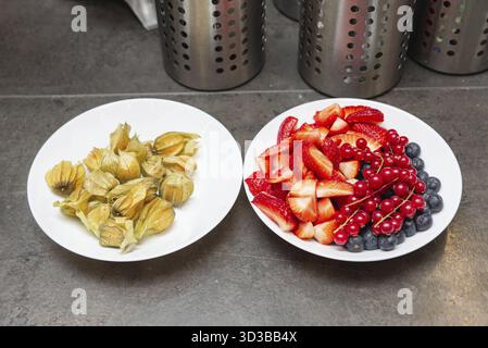 Cibo, due piatti bianchi con frutta assortita: Uno con fragole a fette, mirtilli, ribes rossi, l'altro con fisi intera Foto Stock