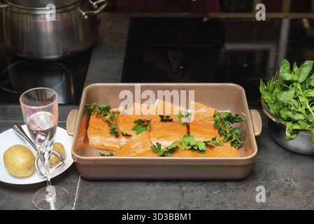 Cibo, filetti di salmone crudi freschi disposti in un piatto da forno con prezzemolo, pronti per la cottura, circondati da patate e spinaci Foto Stock