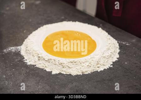 Cibo, farina fresca sistemata in un tumulo con uova sbattute al centro, pronta per essere mescolata per la pasta fatta in casa Foto Stock