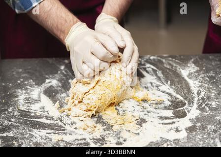 Cibo, primo piano di mani con i guanti impastando la pasta su una superficie infarinata durante il processo di preparazione della cottura in cucina Foto Stock