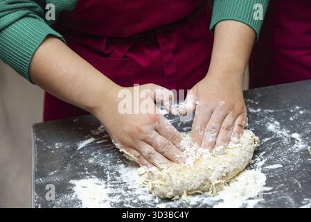 Cibo, primo piano di una persona che impasta l'impasto crudo a mano su un bancone da cucina infarinato, preparandosi per la cottura o la cottura Foto Stock