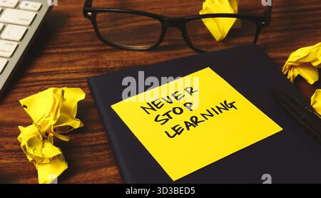 Motivazione per l'apprendimento permanente: Promemoria "non smettere mai di imparare" sulla scrivania con carta sfregata Foto Stock