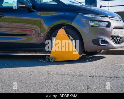 Plymouth, Regno Unito - settembre 25 2025: Morsetto per ruota giallo brillante su un'auto dopo un parcheggio illegale a Plymouth, Regno Unito. Primo piano nella luce del pomeriggio enfatizza l'applicazione e le sanzioni per il parcheggio. Foto Stock
