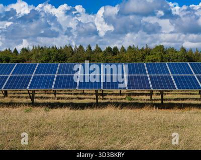 Somerset, Regno Unito - 04 settembre 2025: File di pannelli fotovoltaici commerciali si estendono attraverso un campo erboso sotto nuvole drammatiche a Somerset, Regno Unito, catturando clea Foto Stock