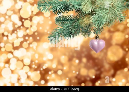 Ramo dell'albero di Natale con palla a forma di cuore contro luci sfocate, effetto bokeh Foto Stock
